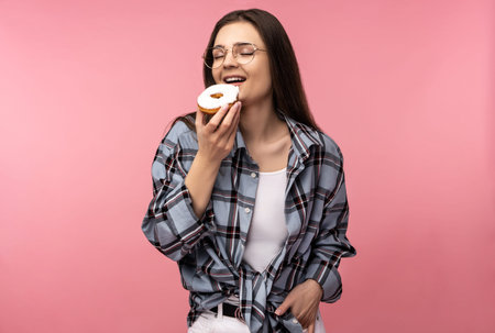 Photo of attractive lady holds eats donut sweet food, wear casual checkered shirt white undershirt...