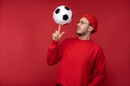 Photo of attractive man with beard in glasses and red clothing. Happy man holds the ball on the index finger, isolated over red backgroundの写真素材