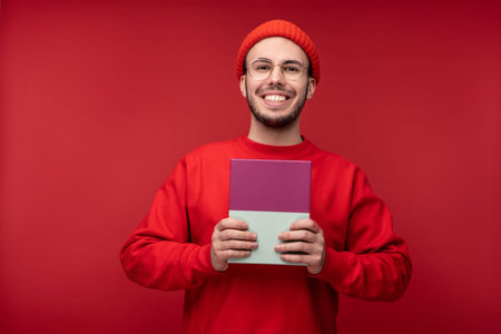 Photo of attractive man with beard in glasses and red clothing. Male holds present in box, isolated...