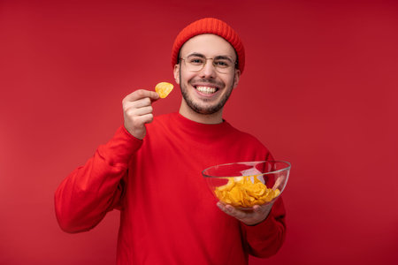Photo of happy man with beard in glasses and red clothing. Holds and eats a plate of chips, isolated...
