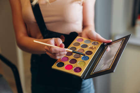 Multi-colored eyeshadow palette close-up. Makeup artist taps the eyeshadow with a brushの写真素材