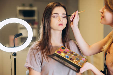 Woman with brown hair and closed eyes does makeup. The makeup artist applies glittering shadows to the eyelidsの写真素材