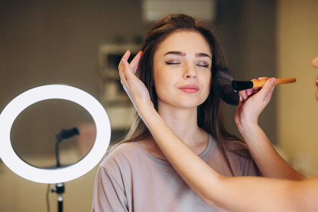 Close-up of a woman with brown hair getting makeup. Makeup brush near the face.