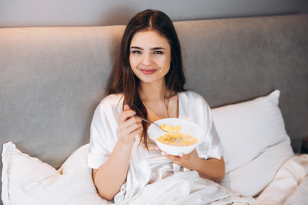 cornflakes for breakfast in bed. beautiful woman holding a plate of cornflakes in bedの写真素材