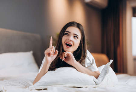 Young beautiful woman has an idea while she is lying on the bed. The female model shows emotionsの写真素材