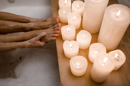 Close up photo of womans body in spa bathtub with wooden table vase of plant candle. Modern spa centerの写真素材