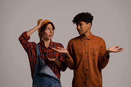 Photo of cute couple farmers look worried about something. White woman wears denim overall, black man shirt isolated brown color backgroundの写真素材
