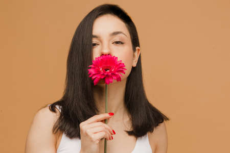 Close up fit and sporty female in underwear. Beautiful and healthy woman is smelling flower, beige background. Sport, fitness, diet, weight loss and healthcare concept.の写真素材