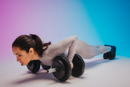 Plank. Young sportive woman training isolated on gradient studio background in neon light. Modern...