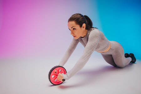 Close up portrait of young fit and sportive caucasian woman with press wheel on gradient background....