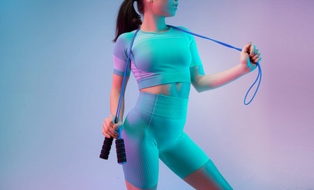 Young fit and sportive woman with rope on gradient background. Fit sportswoman posing, looks...