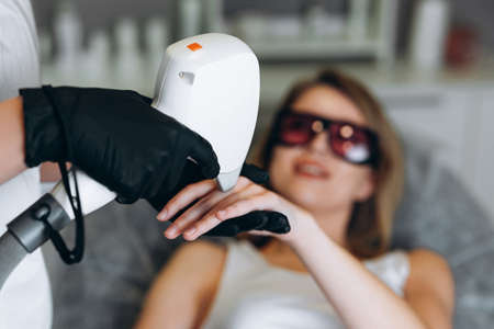 Woman getting laser treatment on her fingers in a beauty salon. Cosmetologist doing laser epilation to her clientの写真素材
