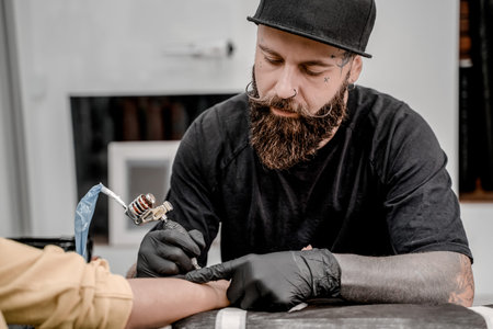 Male tattoo master tattooing female client. Tattoo machine and lamp. Workplace artist. Creating...