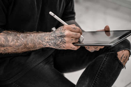 Close-up young man tattoo artist drawing pencil and sketch standing in workshop place. Concept photo of tattoo salonの写真素材