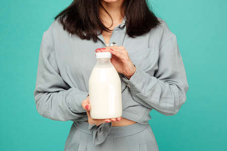 Photo of lady holds bootle of milk, dairy products. Wears grey shirt, isolated turquoise color backgroundの写真素材