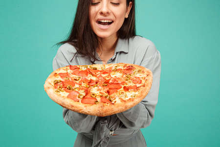 Photo of cute lady holds pizza, enjoy junk food. Wears grey shirt, isolated turquoise color backgroundの写真素材