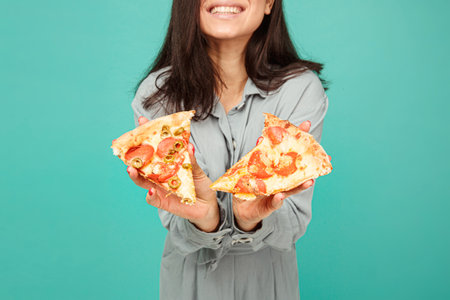 Photo of cute lady shows pizza, enjoy junk food. Wears grey shirt, isolated turquoise color backgroundの写真素材
