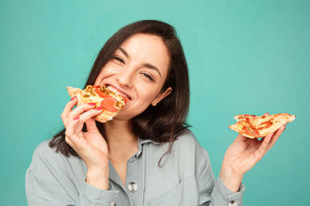 Photo of cute lady eats pizza, enjoy junk food. Wears grey shirt, isolated turquoise color backgroundの写真素材