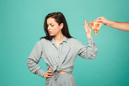 Photo of cute lady is rejecting of eating pizza, healthy lifestyle, no junk food. Wears grey shirt, isolated turquoise color backgroundの写真素材