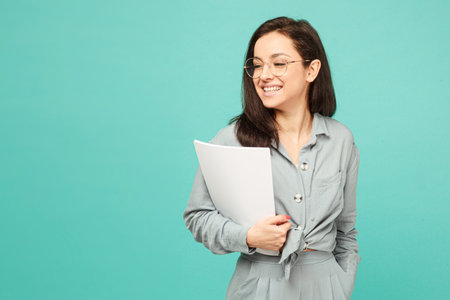 Photo of cute business lady in glasses holds papers. Wears grey shirt, isolated turquoise color...