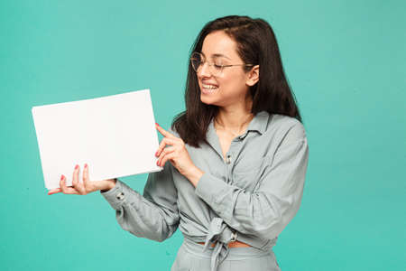 Photo of cute female in glasses holds papers. Wears grey shirt, isolated turquoise color backgroundの写真素材