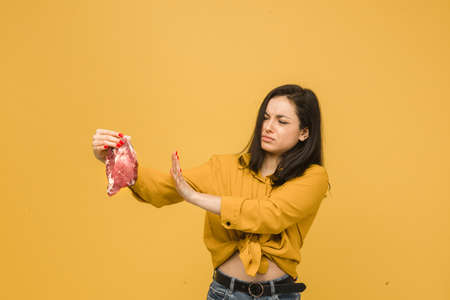 Concept photo of vegetarian female doesn t like meat. Wears yellow shirt, isolated yellow color backgroundの写真素材