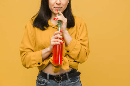 Concept photo of sweet female is drinking cocktails, summertime. Wears yellow shirt, isolated yellow color backgroundの写真素材
