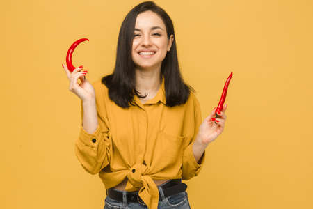Concept photo of young female holds red paper, looks like she love spicy food. Wears yellow shirt, isolated yellow color backgroundの写真素材