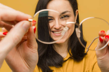 Close up photo of young female through glasses. Wears yellow shirt, isolated yellow color backgroundの写真素材