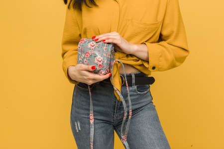 Close up photo of young female holds her purse. Wears yellow shirt, isolated yellow color backgroundの写真素材
