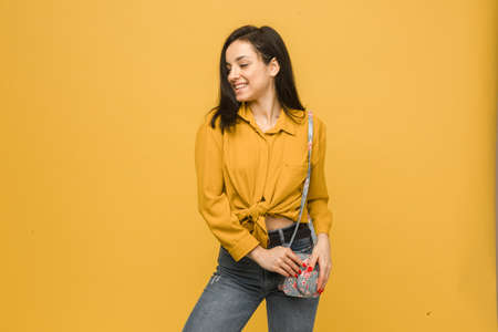 Concept photo of young female with purse, smiling and looks happy. Wears yellow shirt, isolated yellow color backgroundの写真素材