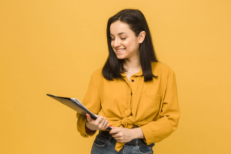 Concept photo of business lady holds papers. Wears yellow shirt, isolated yellow color backgroundの写真素材
