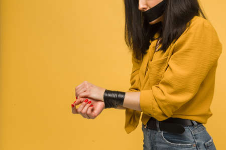 Photo of cute female victim with her mouth taped up, kidnapping. Wears yellow shirt, isolated yellow color backgroundの写真素材