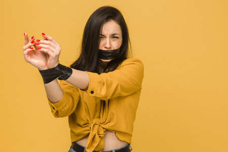 Photo of poor female victim with her mouth taped up, kidnapping. Wears yellow shirt, isolated yellow color backgroundの写真素材