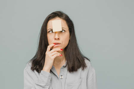 Photo of cute smiling female with sticker over her forehead. Wears grey shirt, isolated grey color backgroundの写真素材