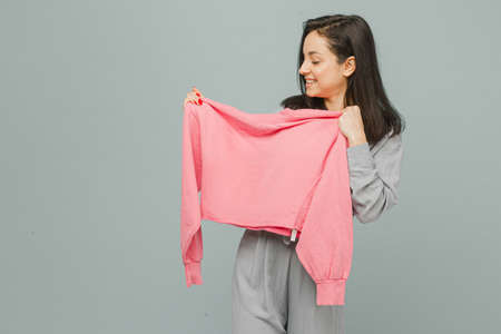 Photo of cute smiling female holds pink sweater. Wears grey t-shirt, isolated grey color backgroundの写真素材