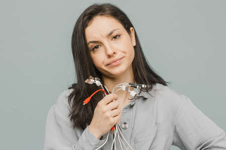 Photo of cute female disappointed of broken chargers. Wears grey dress, isolated grey color backgroundの写真素材