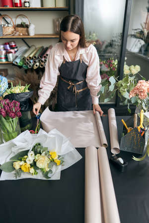 Female florist holding decorative Kraft beforehand making bouquet, in flower shop.の写真素材