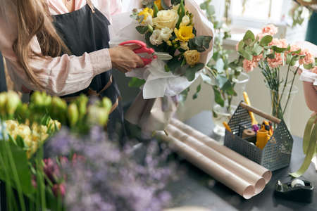 Portrait of successful modern florist wearing apron, creating beautiful bouquet of colorful different flowers in modern interior floral shop. Close up.の写真素材