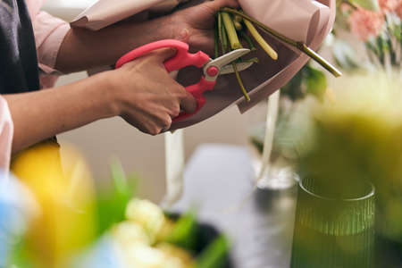 florist creating beautiful bouquet in flower shop, close up. cutting branches.の写真素材