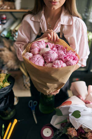 Close-up image of female florist making beautiful bouquet of fresh flowers. Portrait of successful modern florist wearing apronの写真素材
