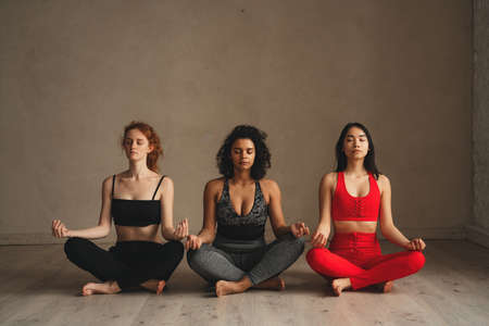 Fit athletic women doing meditation, healthy lifestyle. Beautiful women working out in gym together. Intense fitness training workout in loft industrial gymの写真素材