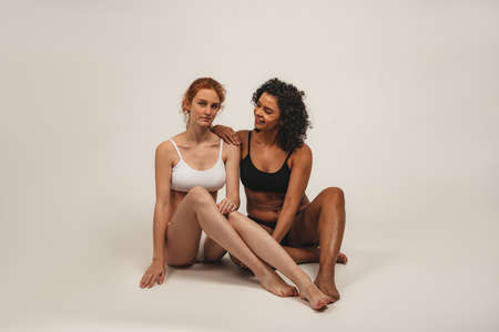 Photo of natural multiracial women, body positive. Feminist females in underwear sit, isolated on white background. Concept natural beauty and girl powerの写真素材