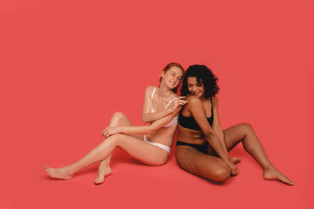Photo of natural and cute multiracial women, body positive. Feminist females sit isolated on pink background. Concept natural beauty and girl powerの写真素材