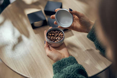 Female hand holds bowl of ground coffee and beans in gift box on the tableの写真素材