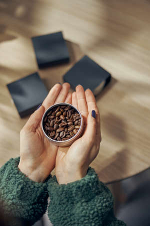 Female hand holds bowl of ground coffee and beans in gift box on the table, close upの写真素材