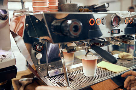 Espresso pouring from coffee machine in cardboard cup. Professional coffee brewingの写真素材