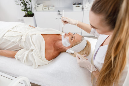 Face peeling mask, spa beauty treatment, skincare. Senior woman getting facial care by beautician at...