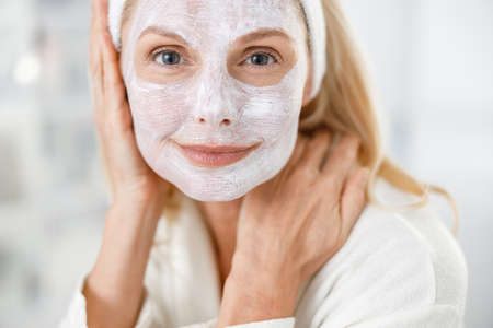 Close up of senior blond woman with nutrition mask on her face, visiting cosmetologists in modern medical centerの写真素材