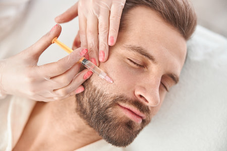 Close up makes mesotherapy injections to young man. Treatment of male by a beautician for tightening and smoothing wrinkles on the face skinの写真素材